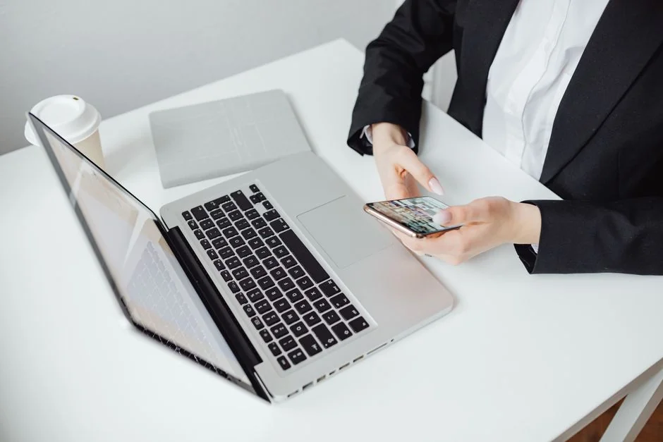 Person analyzes stock data with a smartphone and laptop, indoors.